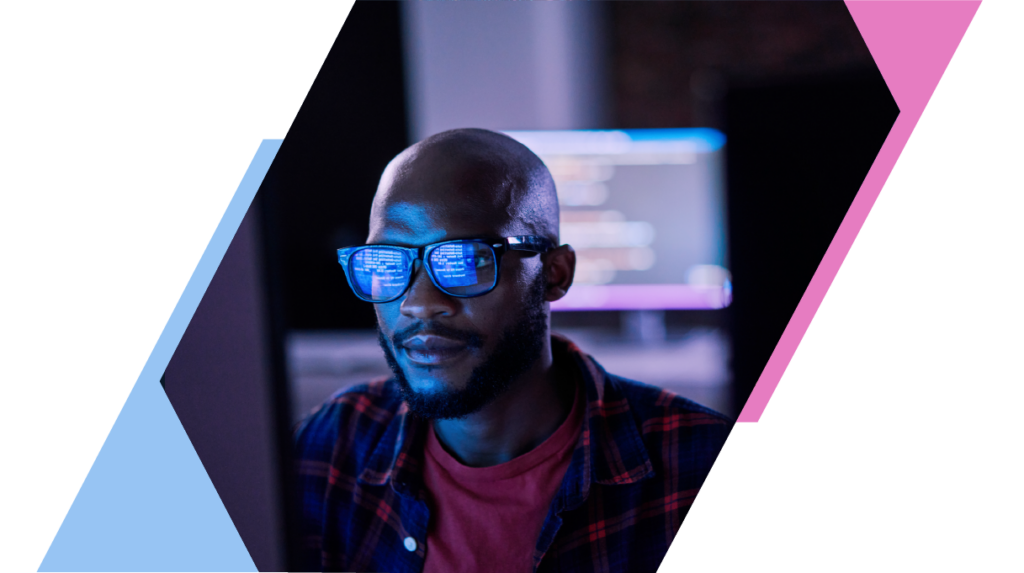 Man coding at a computer with code reflecting on his glasses, surrounded by modern, angular blue and pink design.