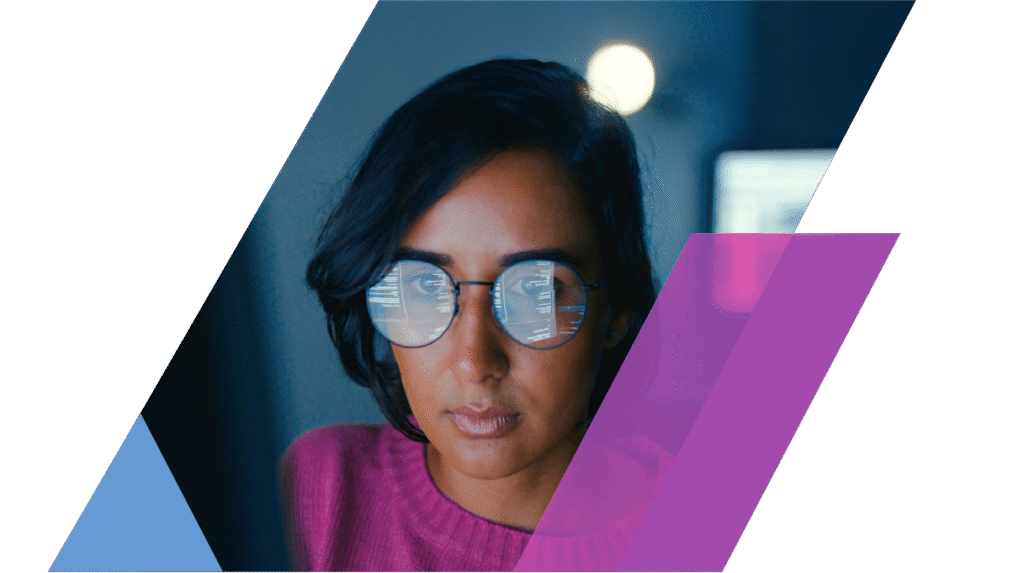 A woman wearing glasses focuses intently on a computer screen, visible code reflected in her lenses.