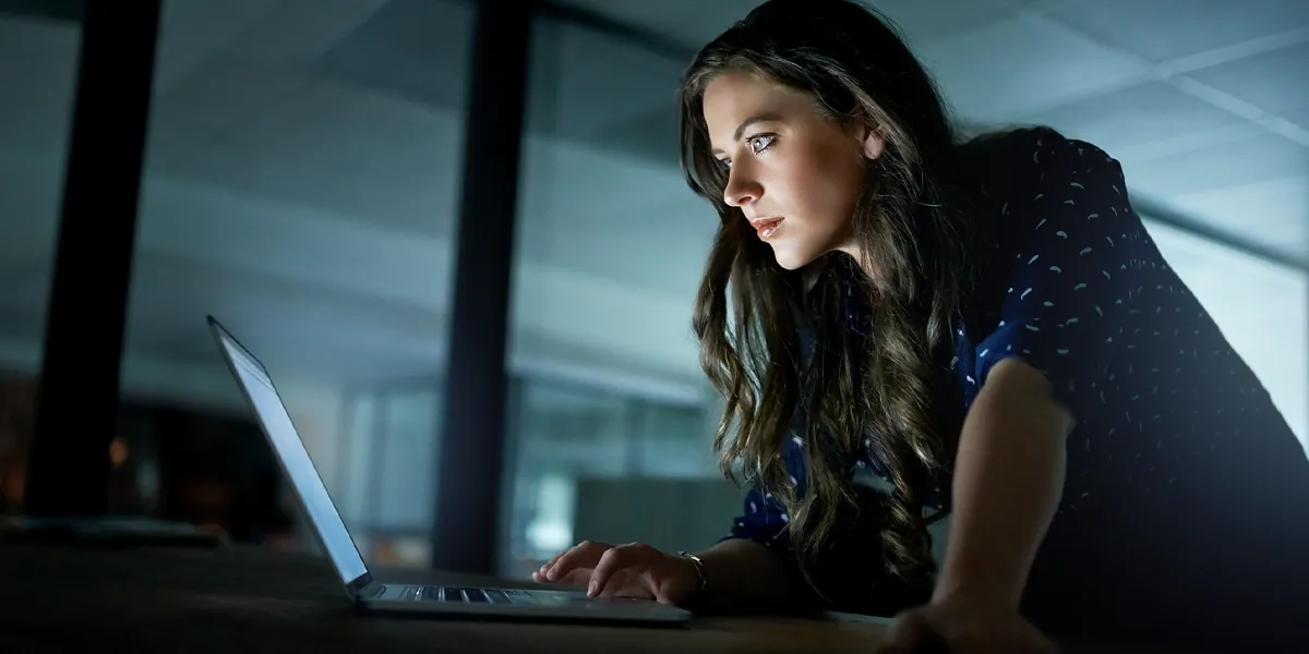 Women sitting at a desk looking at a laptop in a dark room